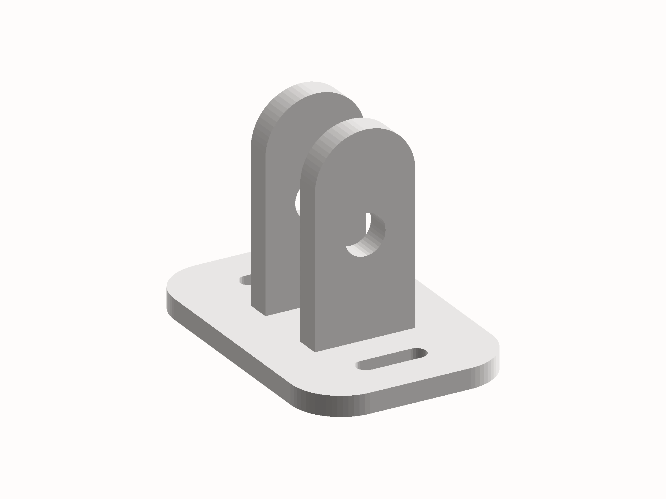 Shaded render of the pulley mount: a slotted base plate with two rounded upright tabs, each pierced by an axle hole.